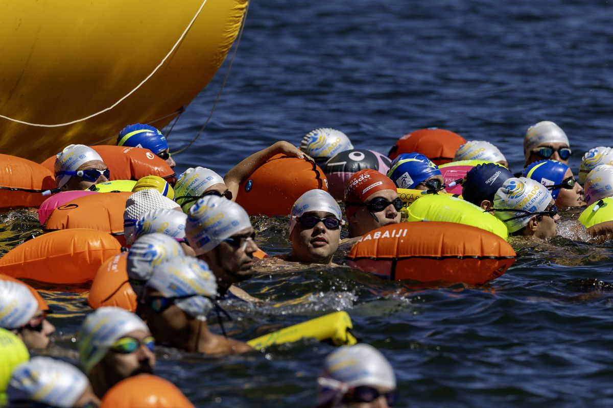 Nadadores aguardam na água entre boias coloridas antes da largada no lago