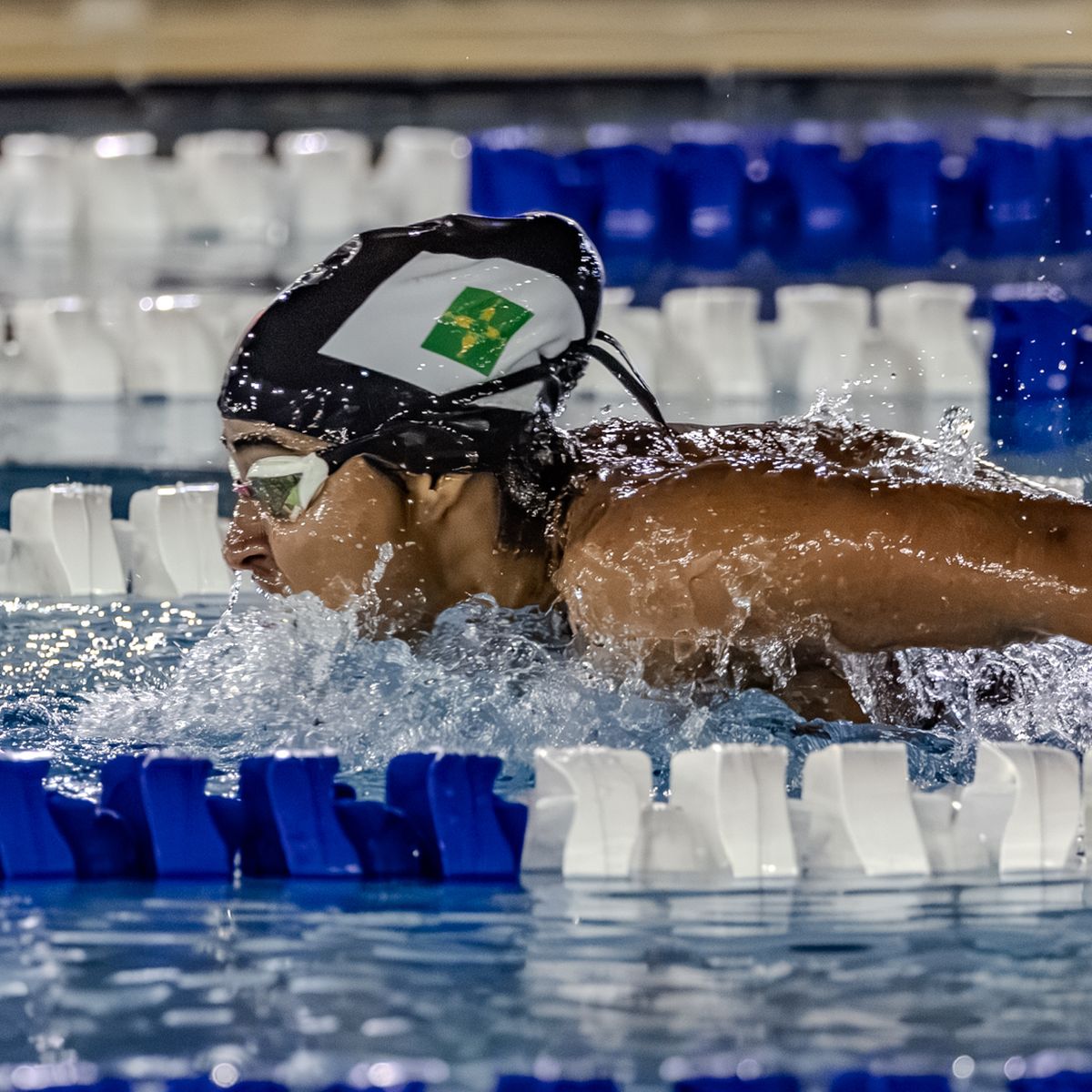 Nadador com touca do Distrito Federal nada borboleta em piscina de competição