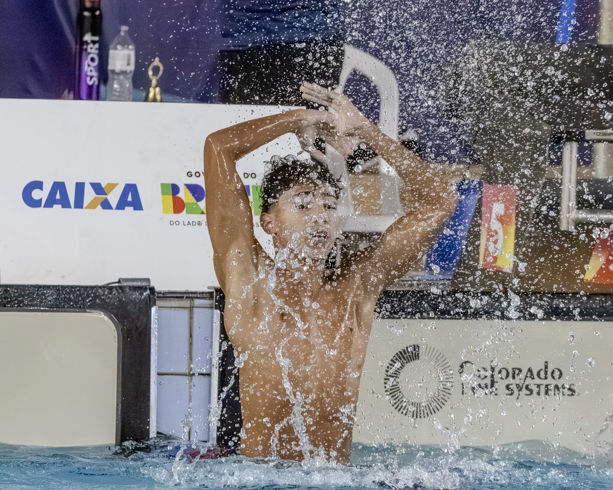 Nadador comemora dentro da piscina após a chegada, com respingos de água ao redor
